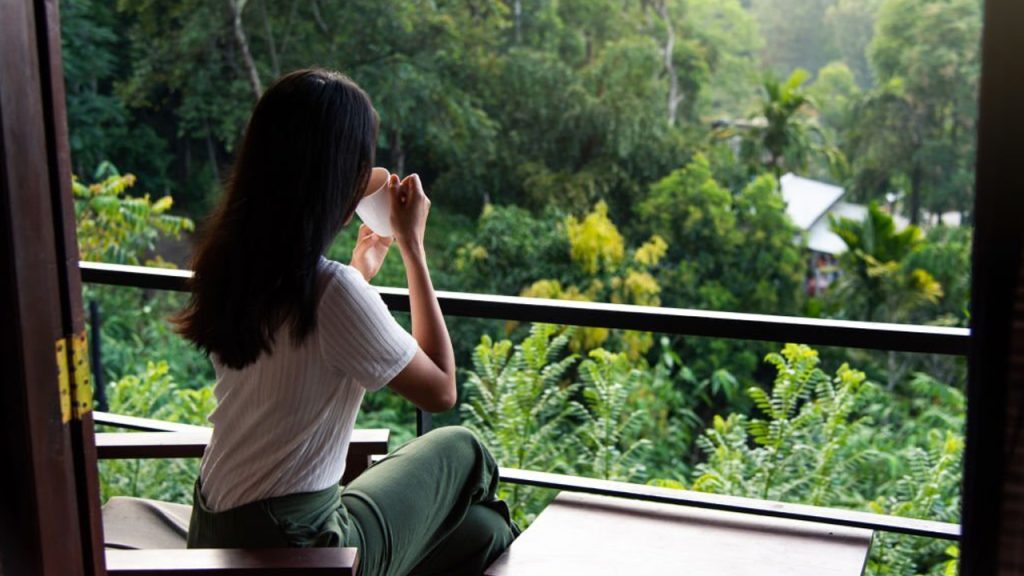 A girl is drinking from the cup and enjoying the view from the balcony.
